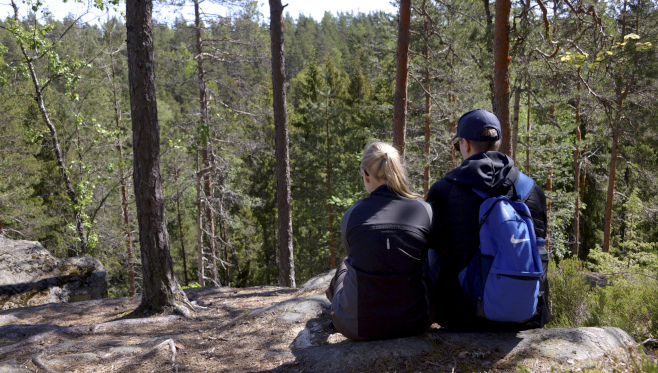 Nuoripari istumassa metsämaisemassa